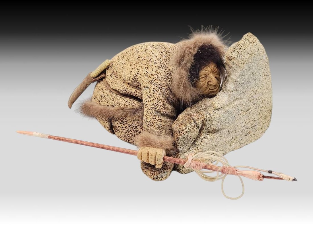 Fossilized Whale Bone Hunter Diorama - Richard Miller: A handsome fossilized whale bone diorama depicting an Alaska Native hunter crouched behind a whale bone protrusion. The hunter, with incised bone face, is accented with fur hair and parka ruff, with b