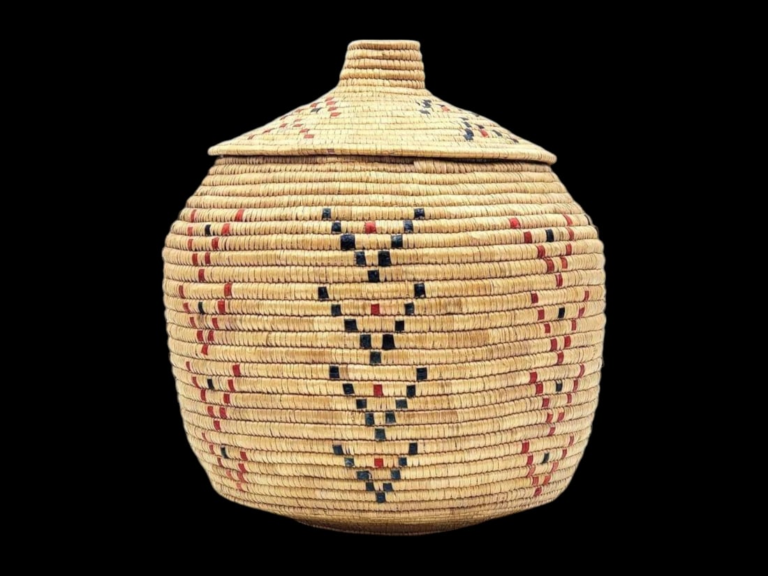 Large Yup'ik Coiled Grass Lidded Basket: A generously sized Yup'ik coiled grass basket featuring a wide base and form-fitting lid with coiled knob finial. Polychrome chevron dyed seal gut accents on the sides and lid retain their vibrant
