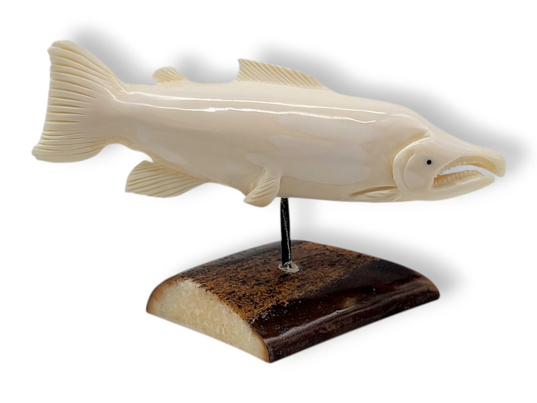 Walrus Tusk Carving of a Swimming Salmon: A walrus tusk carving depicting a swimming salmon with inset baleen eyes, further mounted upon a baleen rod and segment of fossilized tusk base. Initialed R.H.P on the underside by the artist, the pie