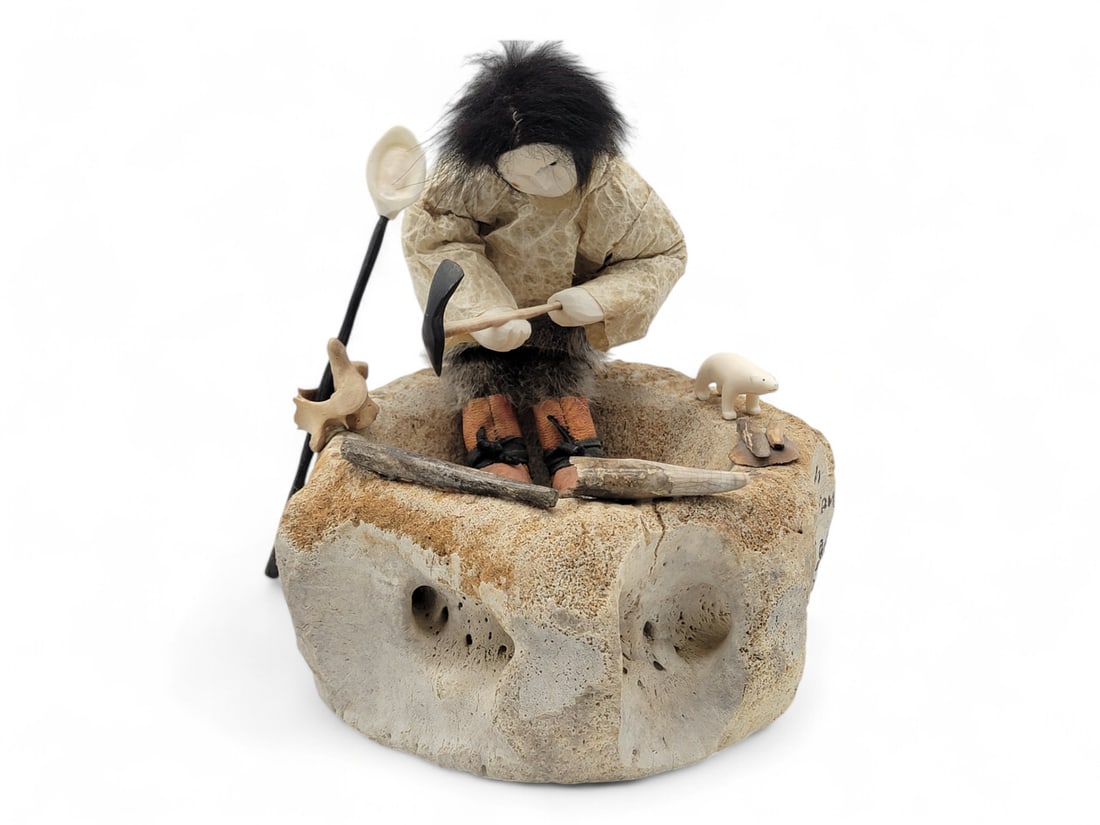 Artifact Digger Story Doll - Beulah Oittillian: A story doll depicting a digger who is sitting on a fossilized whale vertebra excavated from an old village near Gambell on St. Lawrence Island, Alaska. His face is carved from walrus tusk, the eyes a