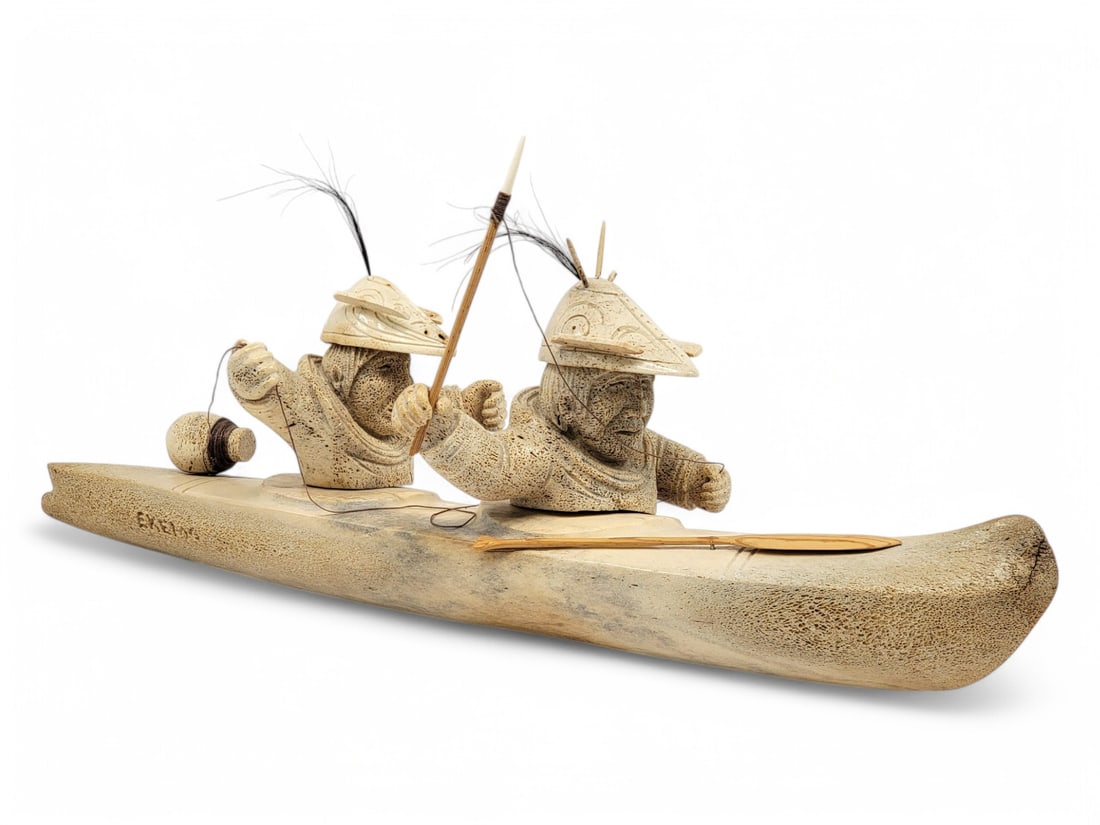 Large Aleut Seal Hunter Sculpture - Ekemo Studios: A highly detailed fossilized whalebone sculpture featuring a pair of Aleut seal hunters in a bidarka, handcrafted by Ekemo Studios of Eagle River, Alaska. The men are attired in walrus bone Qayaatx?ux
