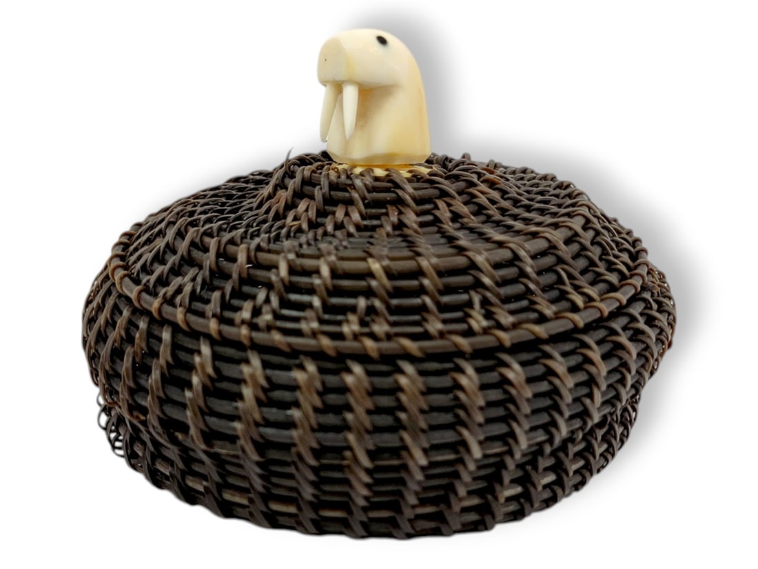 Inupiaq Baleen Basket w/ Walrus Tusk Figural Walrus Head Finial: A squat-shaped Inupiaq baleen basket with wide stitches in shades of black; the domed lid is topped with a walrus tusk finial in the shape of a walrus head; charger base is small within the relatively