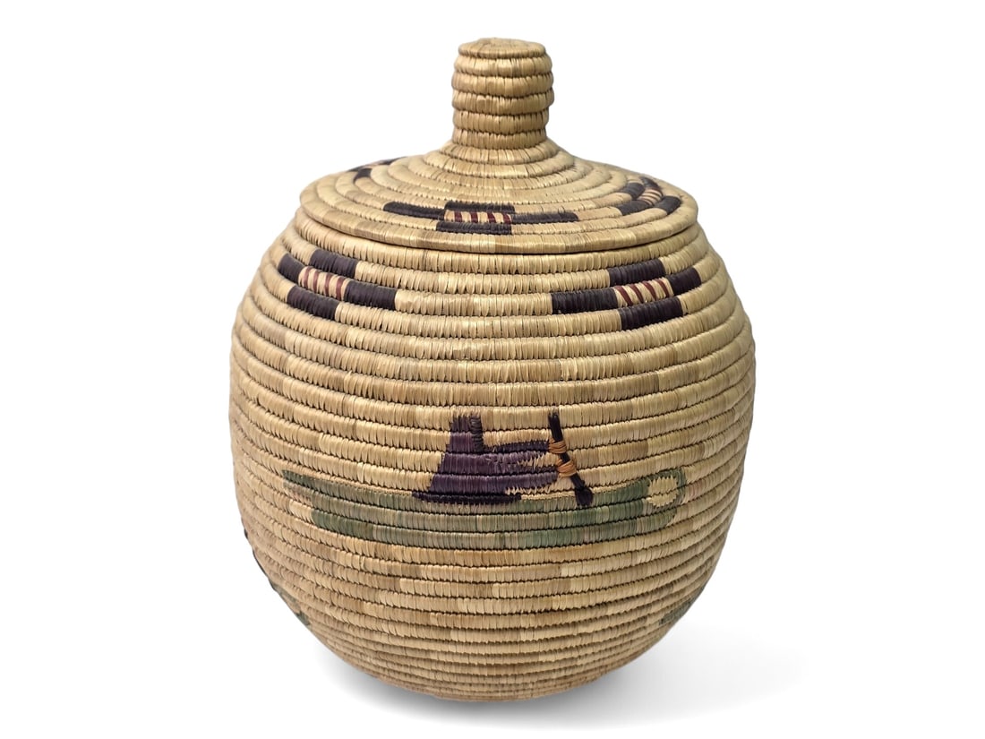 13" Yup'ik Pictorial Woven Grass Basket of Kayaking Scenes: A charming polychrome Yup'ik coiled grass basket of rounded form with gently domed lid and knobbed finial, decorated in dyed grasses with pictorial motifs of a person rowing a kayak around its body, f