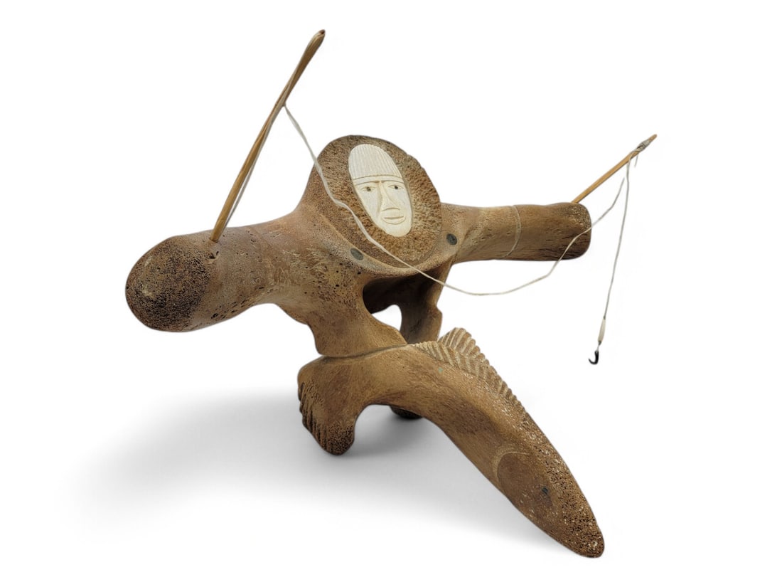 Large Whale Vertebrae Fisherman Sculpture - Ron Ozenna: A fossilized whale vertebrae, fitted with an inset walrus bone face and accented with baleen eyes and shoulder dots. The figure holds a fishing pole with tusk lure and baleen hook, and stands upon a c