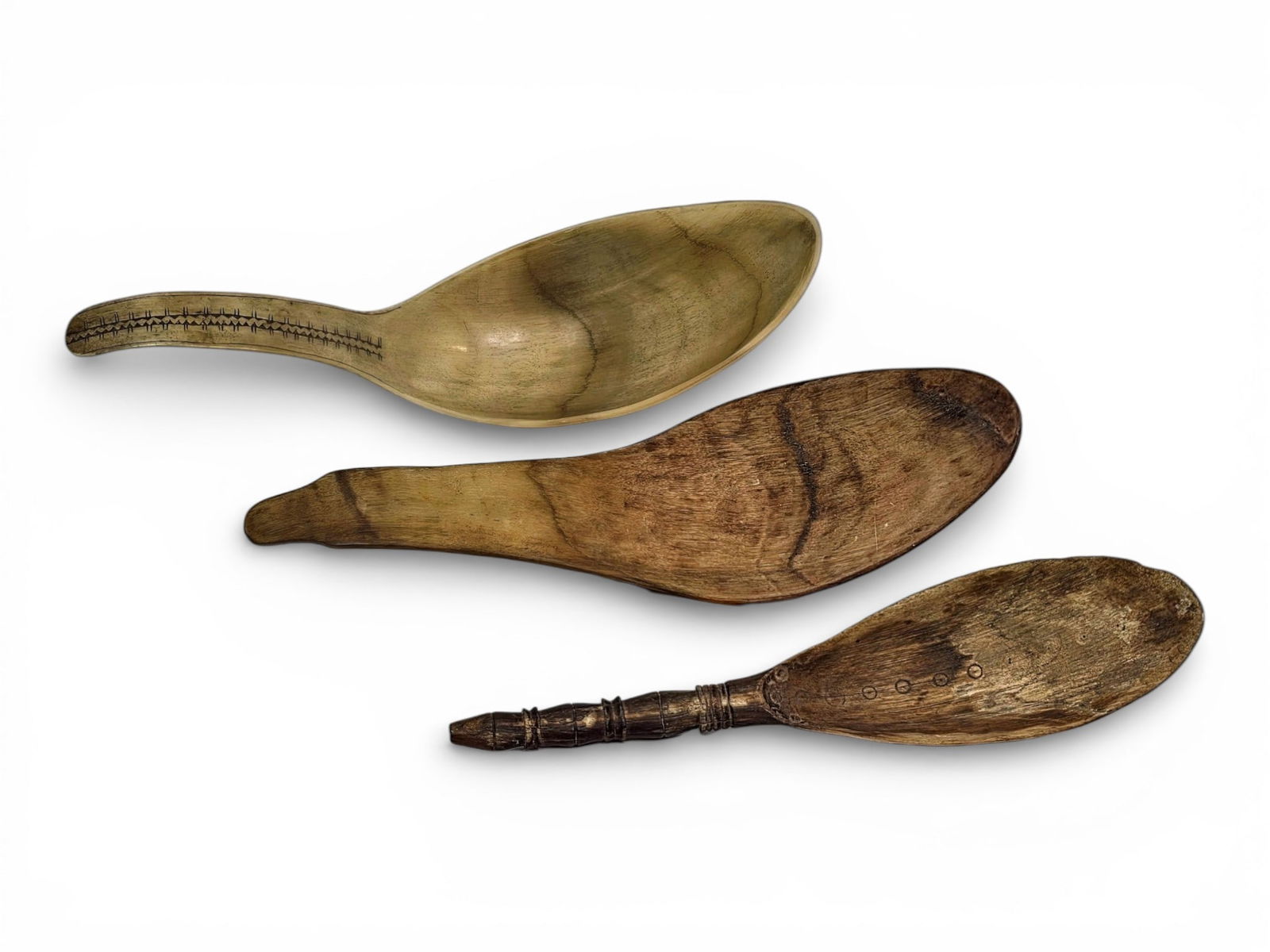 Antique Tlingit & Haida Spoons: A grouping of three late 19th or early 20th century ceremonial serving spoons of Tlingit or Haida origins, one carved wood example with geometric patterns and a detailed handle, plus two sheep horn