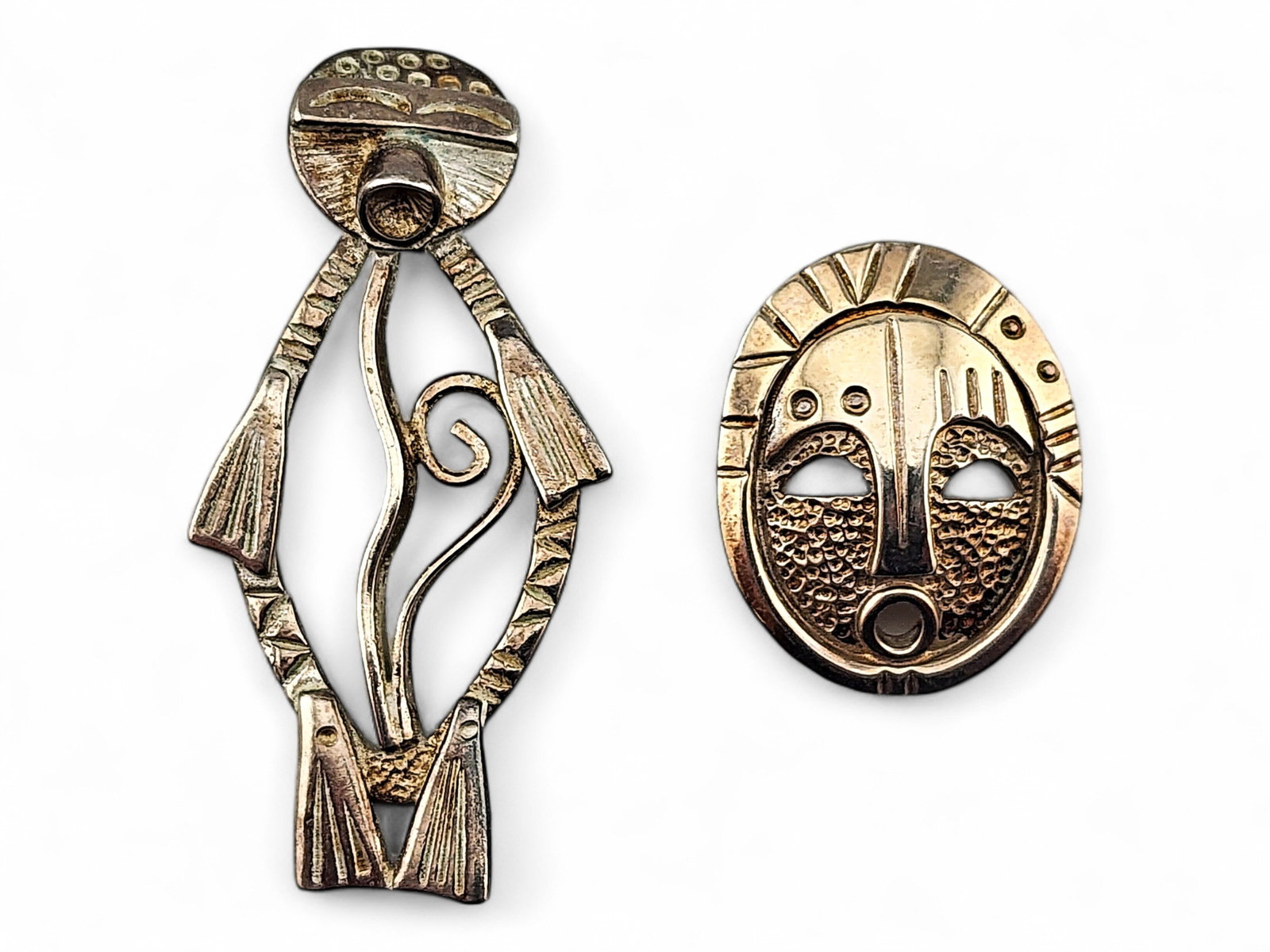 Alaska-Made Sterling Silver Seal & Ceremonial Mask Pendants: Two handcrafted Alaska-made pendants in sterling silver, one depicting a seal with incised flipper and facial details, and one depicting a ceremonial dance mask with hammered and incised features upon