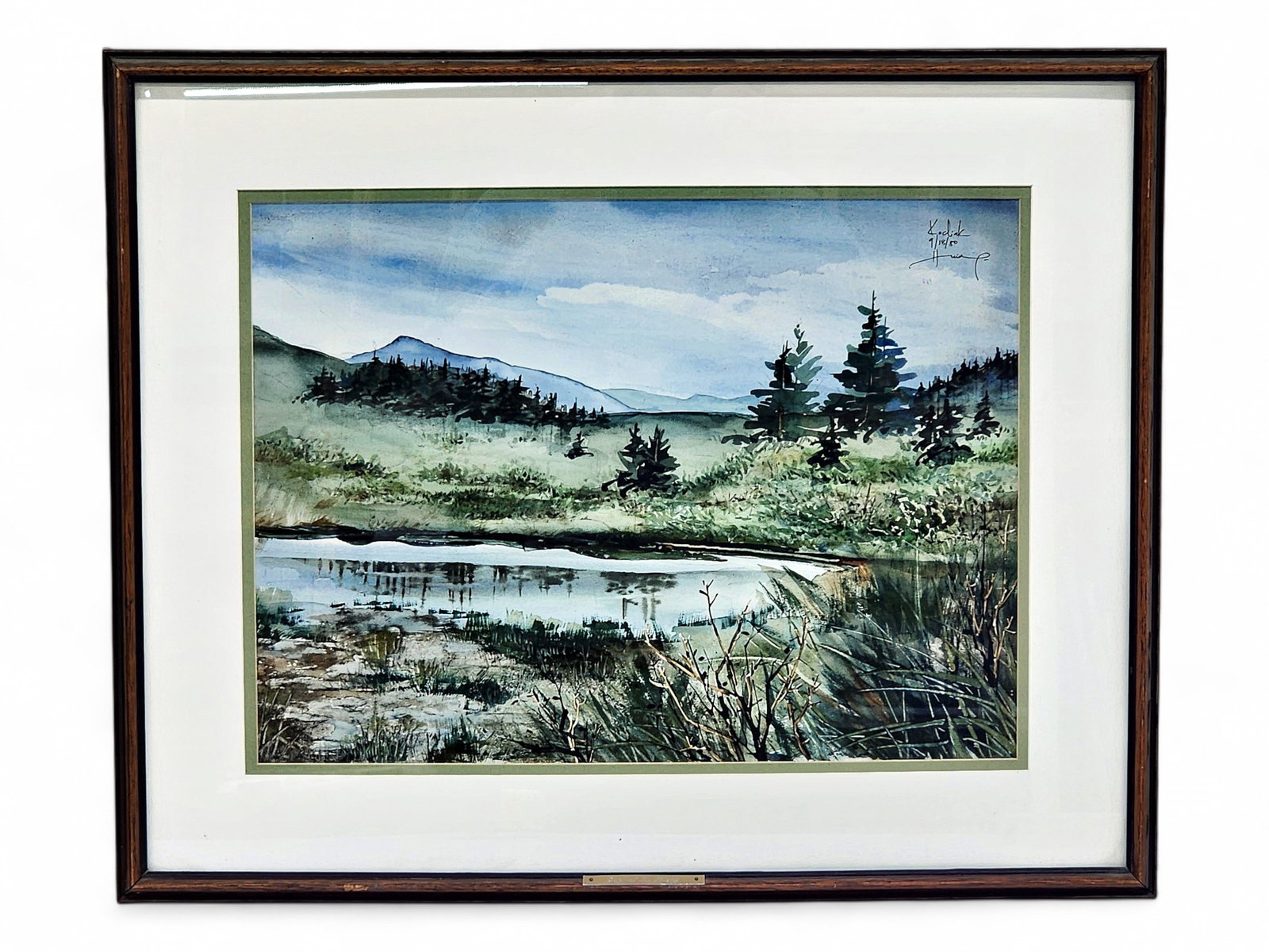 Anna Huöng Alaskan Landscape Watercolor: An original watercolor painting depicting a lake surrounded by evergreen trees and vegetation, with mountain peaks over the horizon in Kodiak, Alaska, signed by Alaska artist Anna Huöng (b.1950) in t