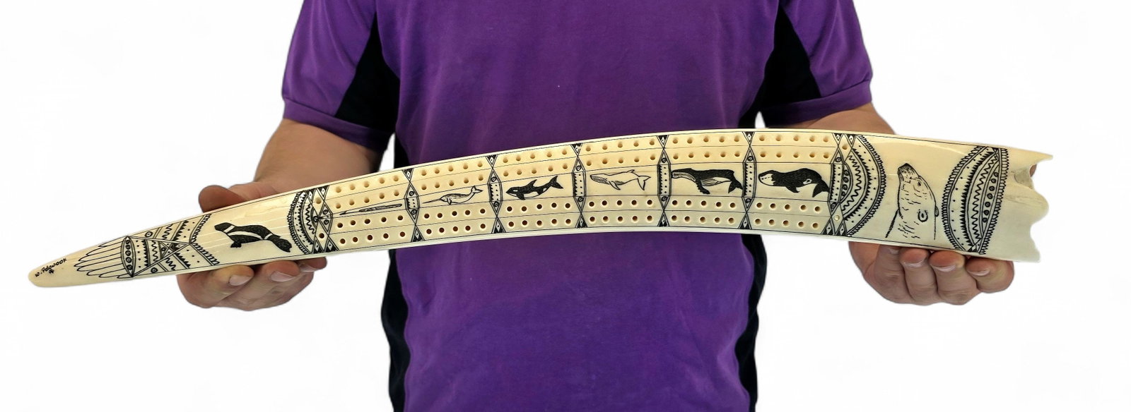 24" Walrus Tusk Cribbage Board - William Pelowook: A walrus tusk cribbage board intricately embellished with an extensive scrimshaw narrative depicting the wildlife and visual traditions of the Arctic. The polished exterior is divided into a series