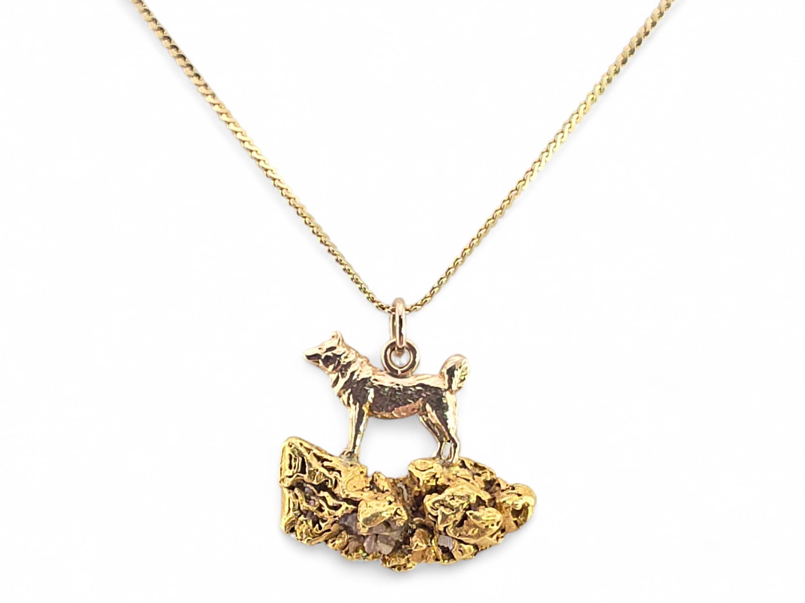 Alaskan Gold Nugget Sled Dog Pendant on 14K Chain: A finely crafted 10-karat yellow gold pendant depicting a sled dog standing atop a rugged outcropping formed from natural Alaskan placer gold nuggets. The polished canine figure, with its curled tail 