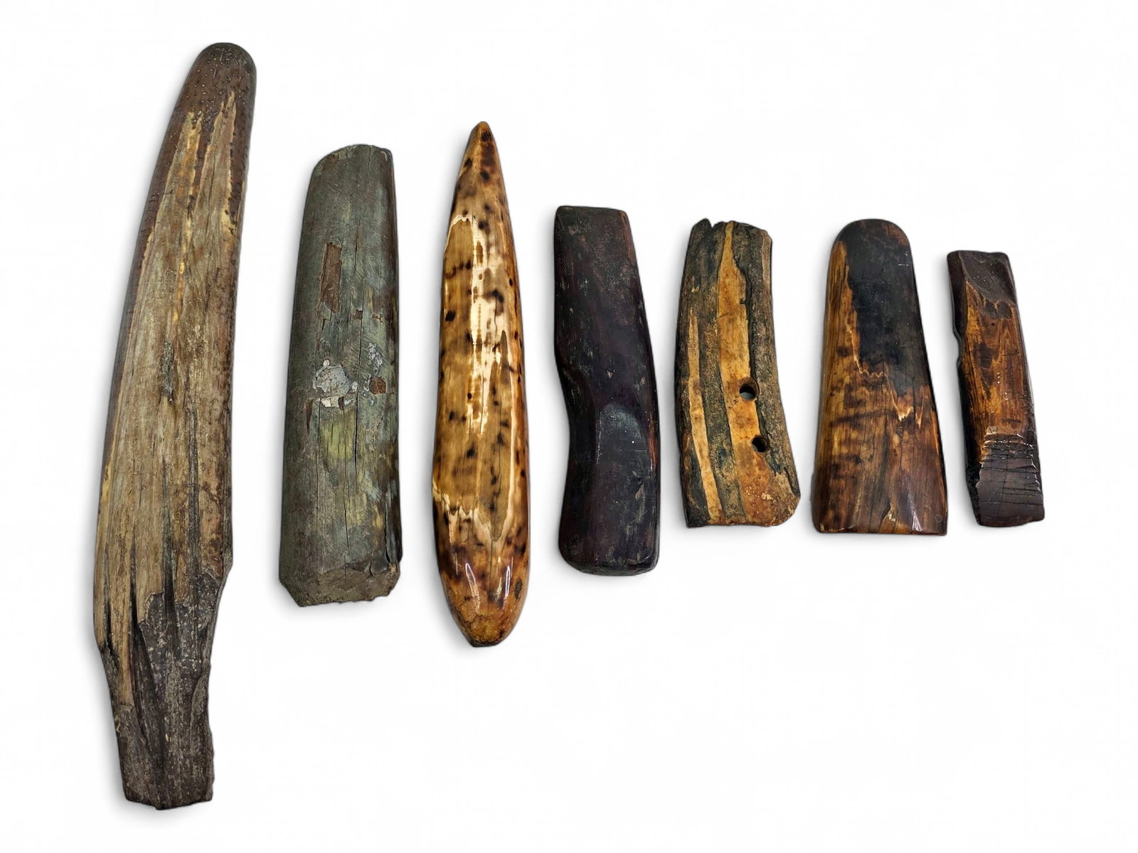 Group of Seven Alaska Native Fossil Walrus Tusk Artifacts: Seven Alaska Native artifacts crafted from fossilized walrus tusk, representing a variety of traditional utilitarian forms including adze heads, wedges, sled runner sections, a weathered fishing weigh