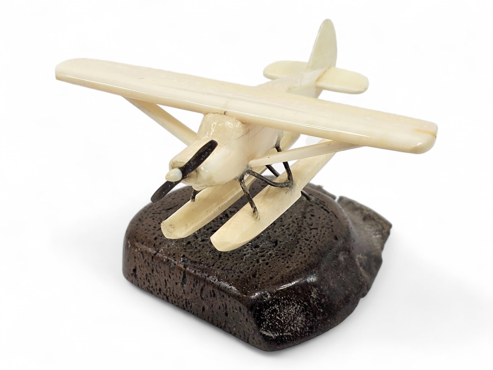 Alaskan Walrus Tusk Float Plane Sculpture: A carved walrus tusk sculpture depicting a classic float plane, inspired by the aircraft that have long served Alaska's remote communities and wilderness regions. The aircraft is skillfully fashioned 