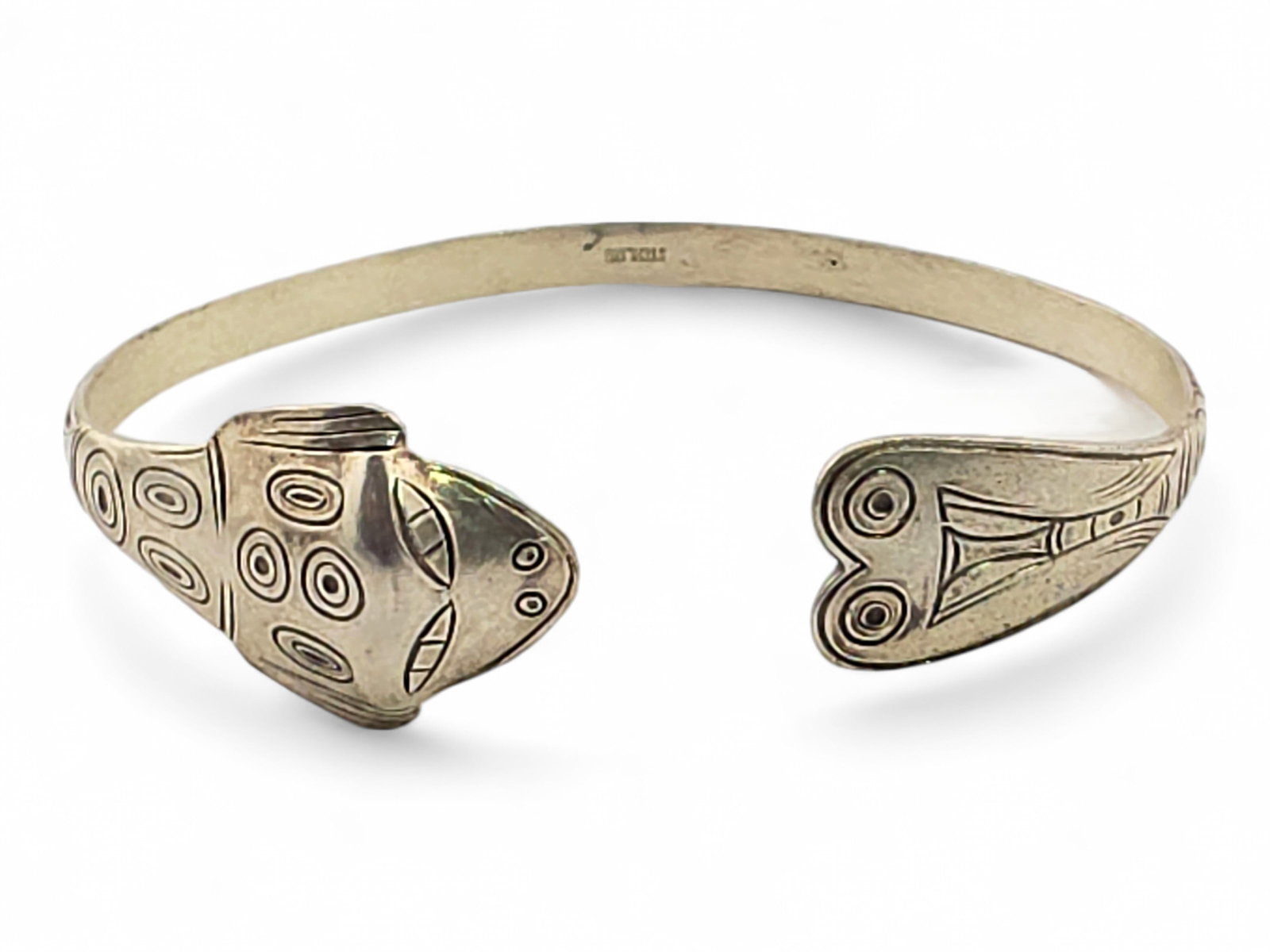 Tlingit Sterling Silver Frog Form Bracelet: A sterling silver cuff bracelet with a stylized formline Tlingit frog motif. The bracelet is formed as a complete frog, with the broad head and prominent ovoid eyes comprising one terminal and the hin