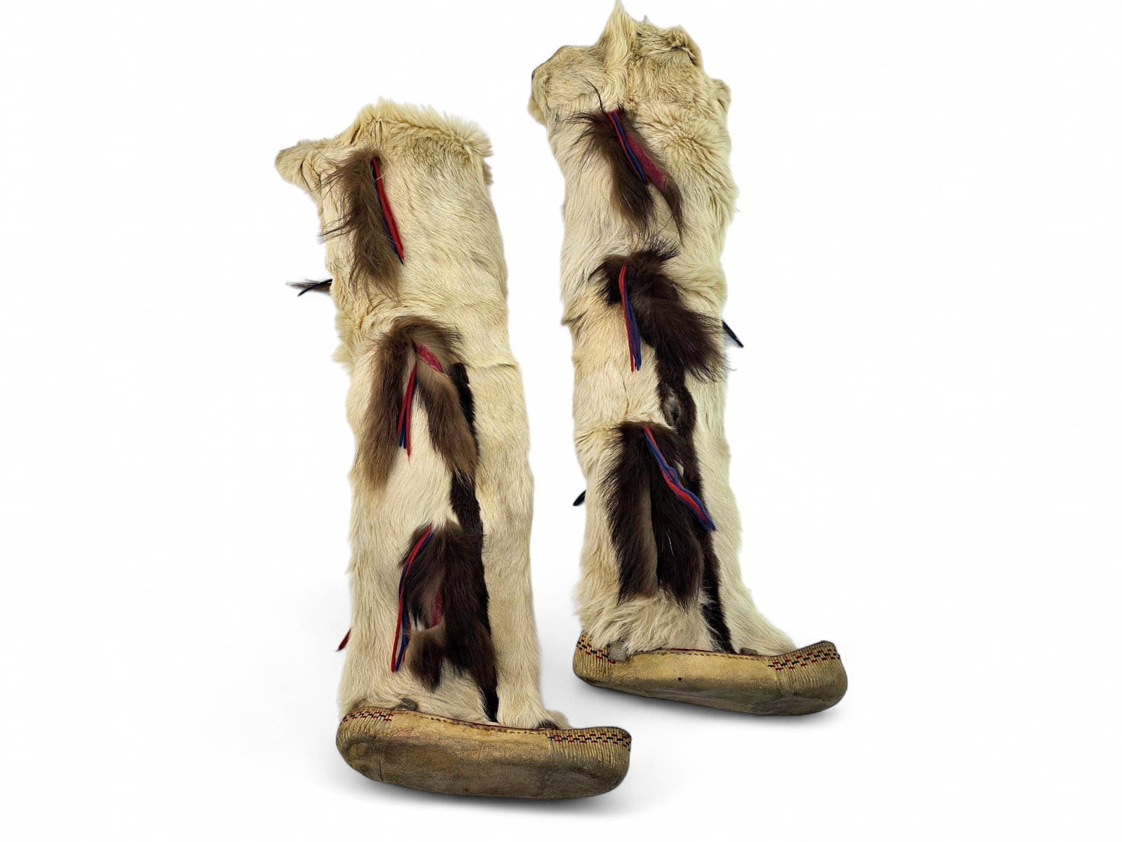 Traditional Alaskan Native Caribou Hide and Fur Knee-High Mukluks: A pair of mid-20th century or earlier Alaskan Native knee-height mukluks, traditionally handcrafted from naturally tanned hide and richly furred caribou pelts. The tall shafts are accented with inset 