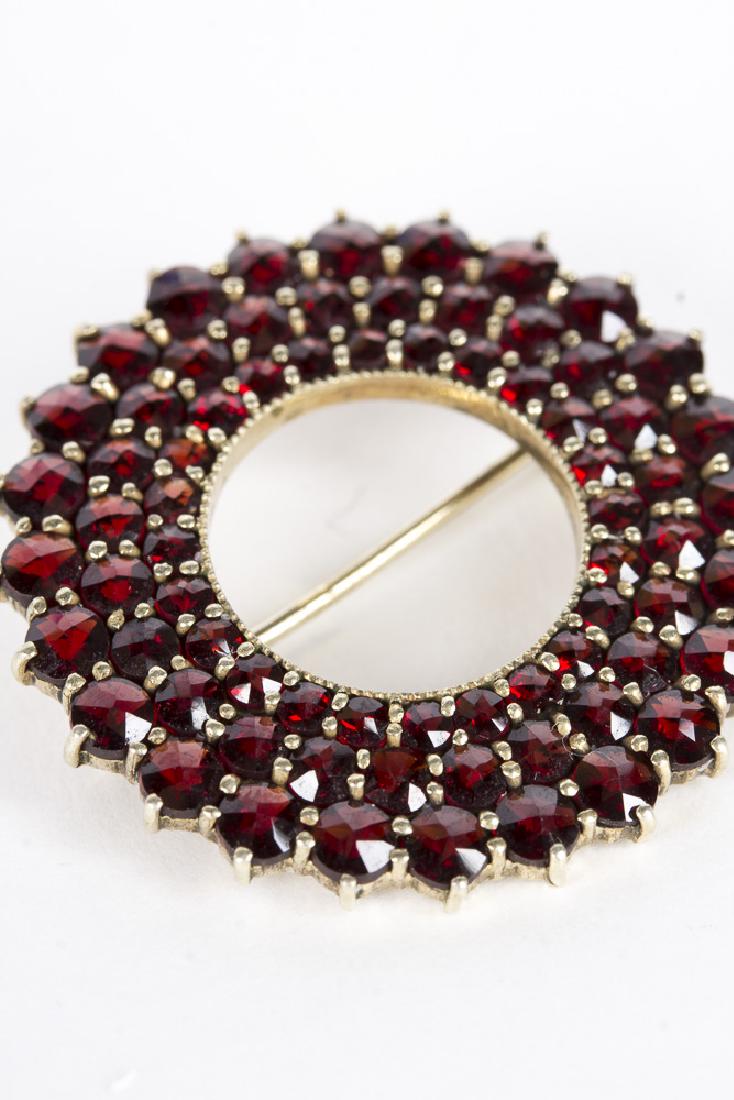 Sterling and garnet wreath brooch: Vintage sterling and garnet wreath brooch. Brooch is composed of 3 concentric rings of garnets, set in sterling silver. A pin adorns the reverse.