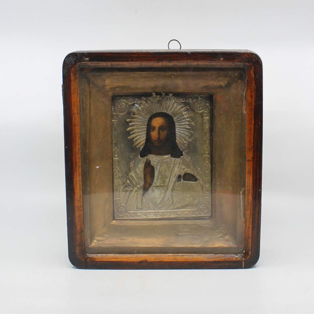 Antique Russian Icon of Jesus in Sterling Oklad: An antique Russian icon with a sterling silver oklad in a hinged glass-front wooden shadow box. This icon depicts Jesus Christ with his right hand raised and his left bearing a cross. He is crowned wi