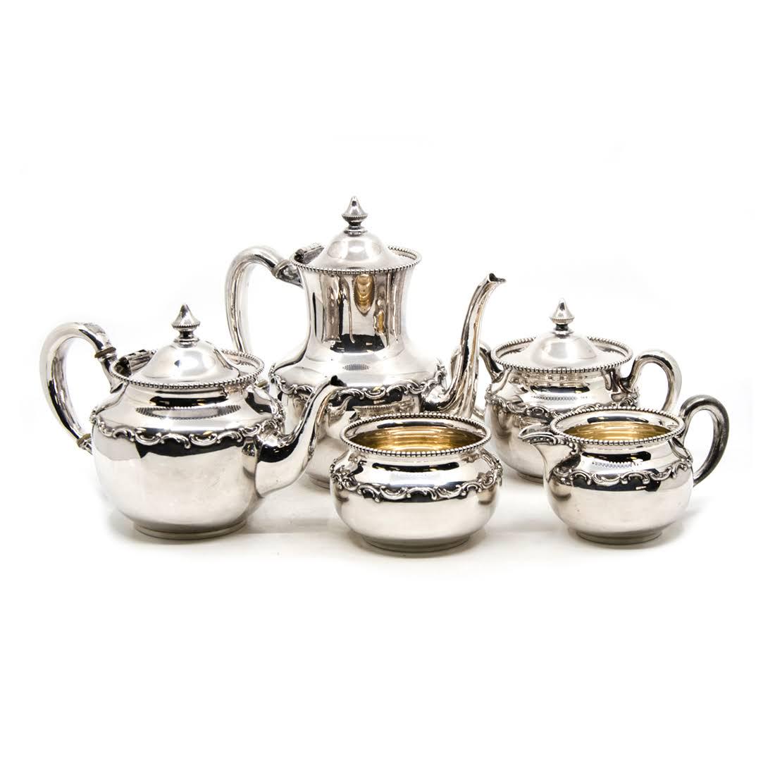 Antique Wallace Nickel Silver Tea and Coffee Service: An antique Wallace nickel silver five piece tea service. Each piece features a raised foliate design around the body and a beaded rim. Each is marked "Wallace Bros Nickel Silver 2318N" on the undersid