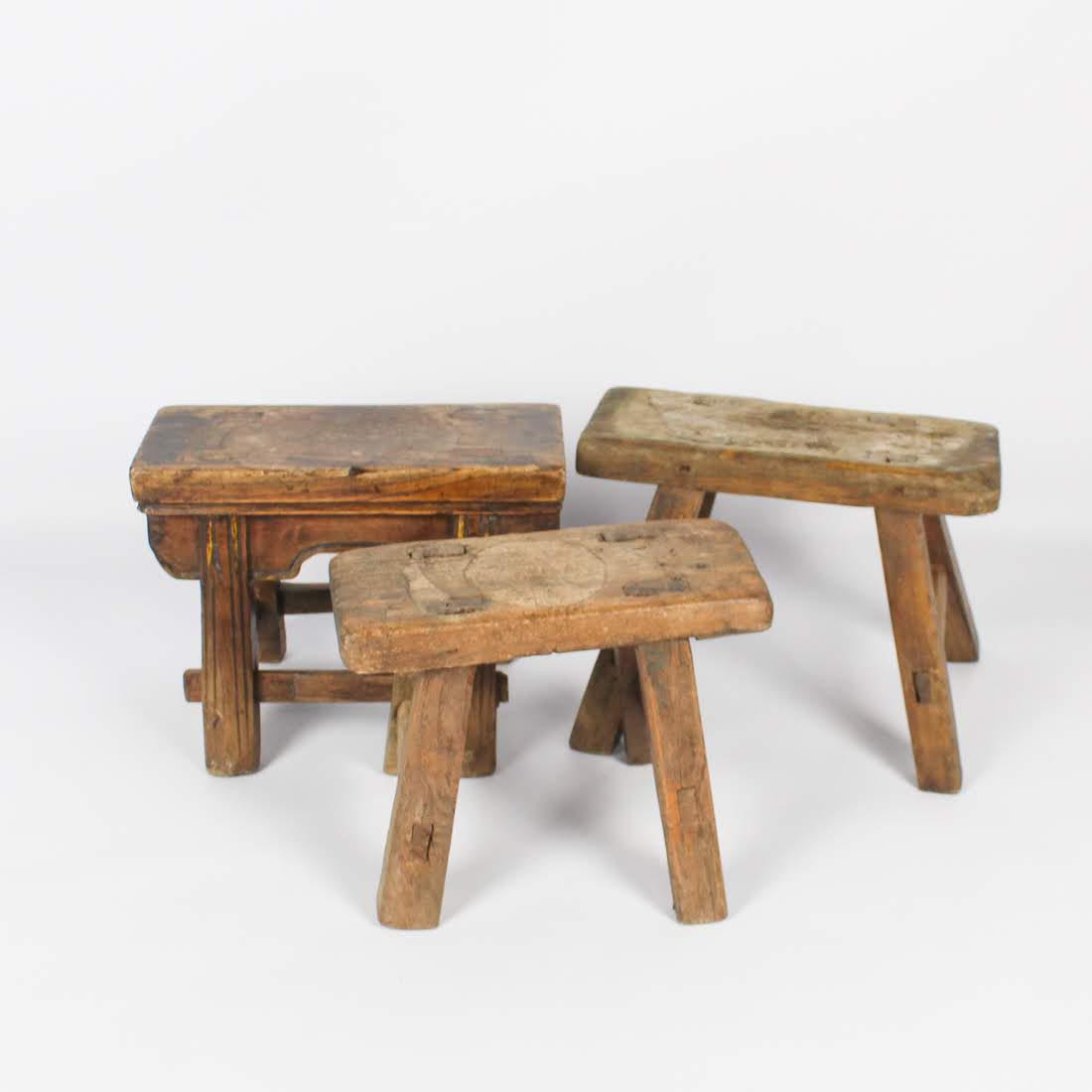 Antique Chinese Primitive Low Milking Stools: A grouping of three antique Chinese low milking stools. Two of the stools feature splayed legs and the other features straight legs, all of which are reinforced with wooden bars. They are unmarked. Di