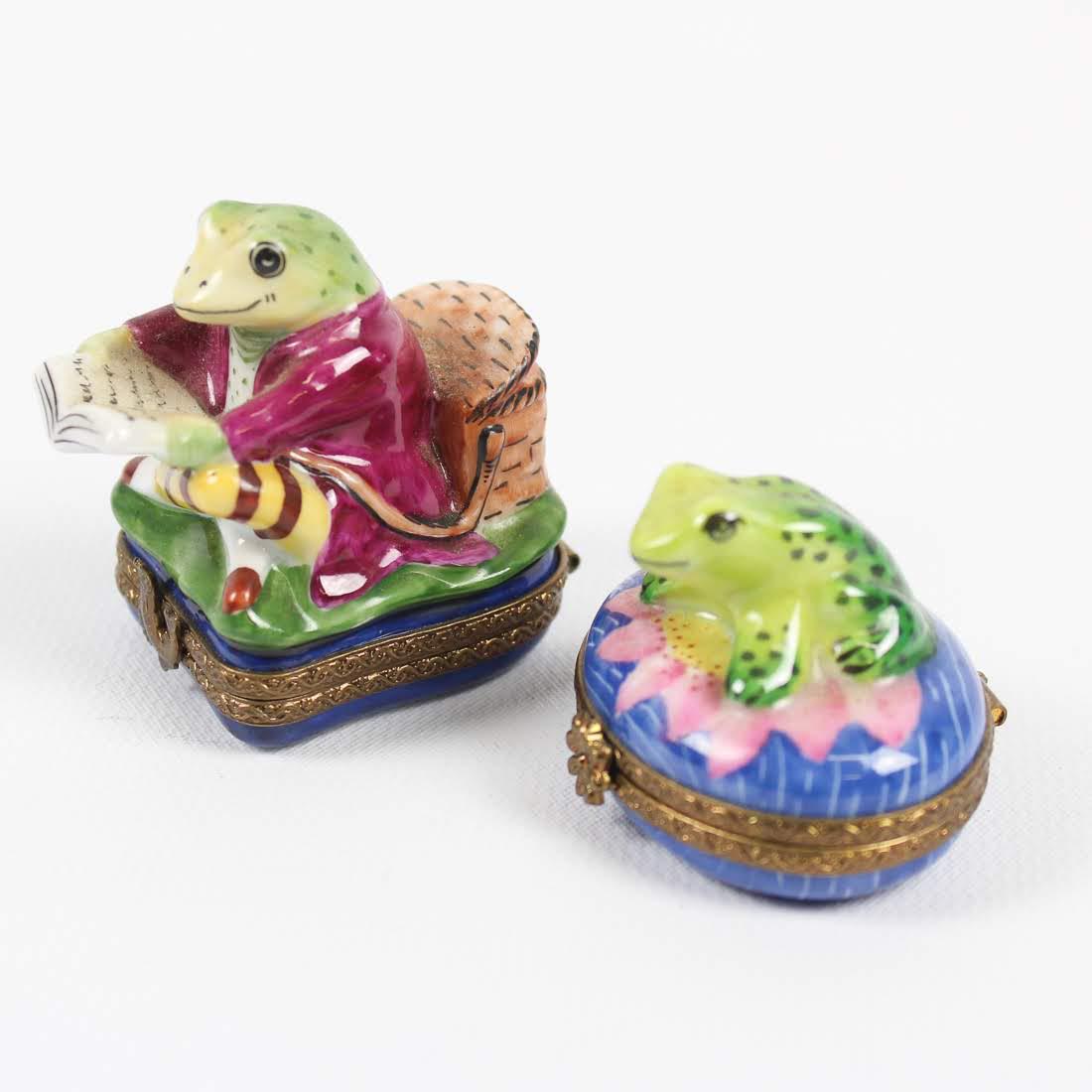 Limoges Peint Main Porcelain Frog Boxes: A grouping of two Limoges Peint Main porcelain boxes. Each box features a frog figure seated atop and is marked on the underside. Dimensions: 2 x 1.25 x 2 Flat Rate Shipping (not calculated):
