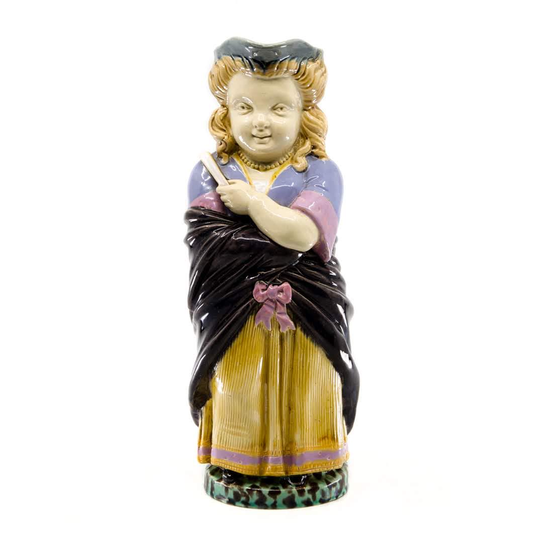 Antique Minton Majolica Peasant Woman Toby Jug: An antique Minton majolica toby jug. This piece takes the form of a peasant woman with a purple and yellow dress, black shawl, hand fan, and grey hat. It is marked "Minton 1140 N" on the underside. Di