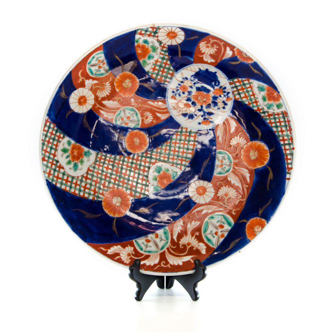 Antique Imari Porcelain Platter: An antique Imari porcelain platter. This piece features a hand-painted swirl design, which joins together at a white circle with a floral vase depiction in the center. The underside of the platter is 