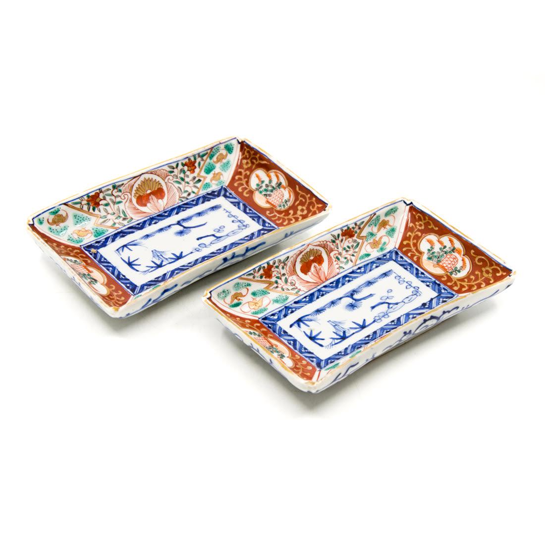 Pair of Antique Imari Hand-Painted Porcelain Dishes: A pair of antique Imari hand-painted porcelain dishes. Each dish features a simple tree design in the center bordered by floral and foliate designs in a palette of red, green, and gold. Each also feat