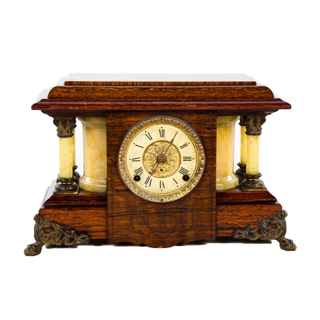 1940s Seth Thomas Burlwood Mantle Clock: A 1940s Seth Thomas burlwood mantle clock. This piece features a Neoclassical design with corinthian columns to either side, a Roman numeral clock face, and ornate brass feet. The clock chimes at half