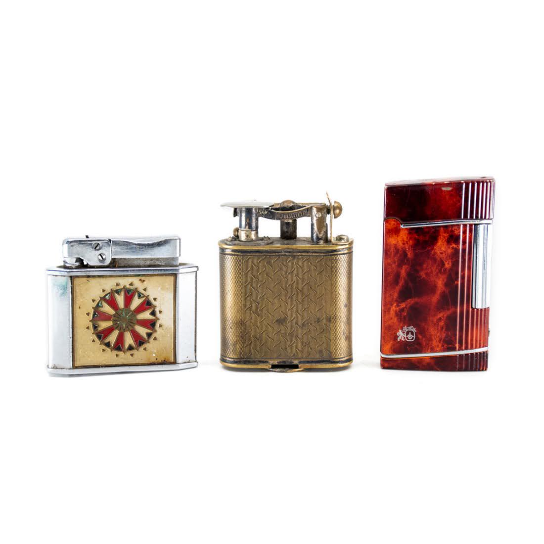 Group of 3 Calibri, Dunhill, and Rogers Lighters: A group of three vintage lighters including a Calibri red marble finish lighter, a Rogers enamel painted dartboard lighter, and a brass plate Dunhill lighter.