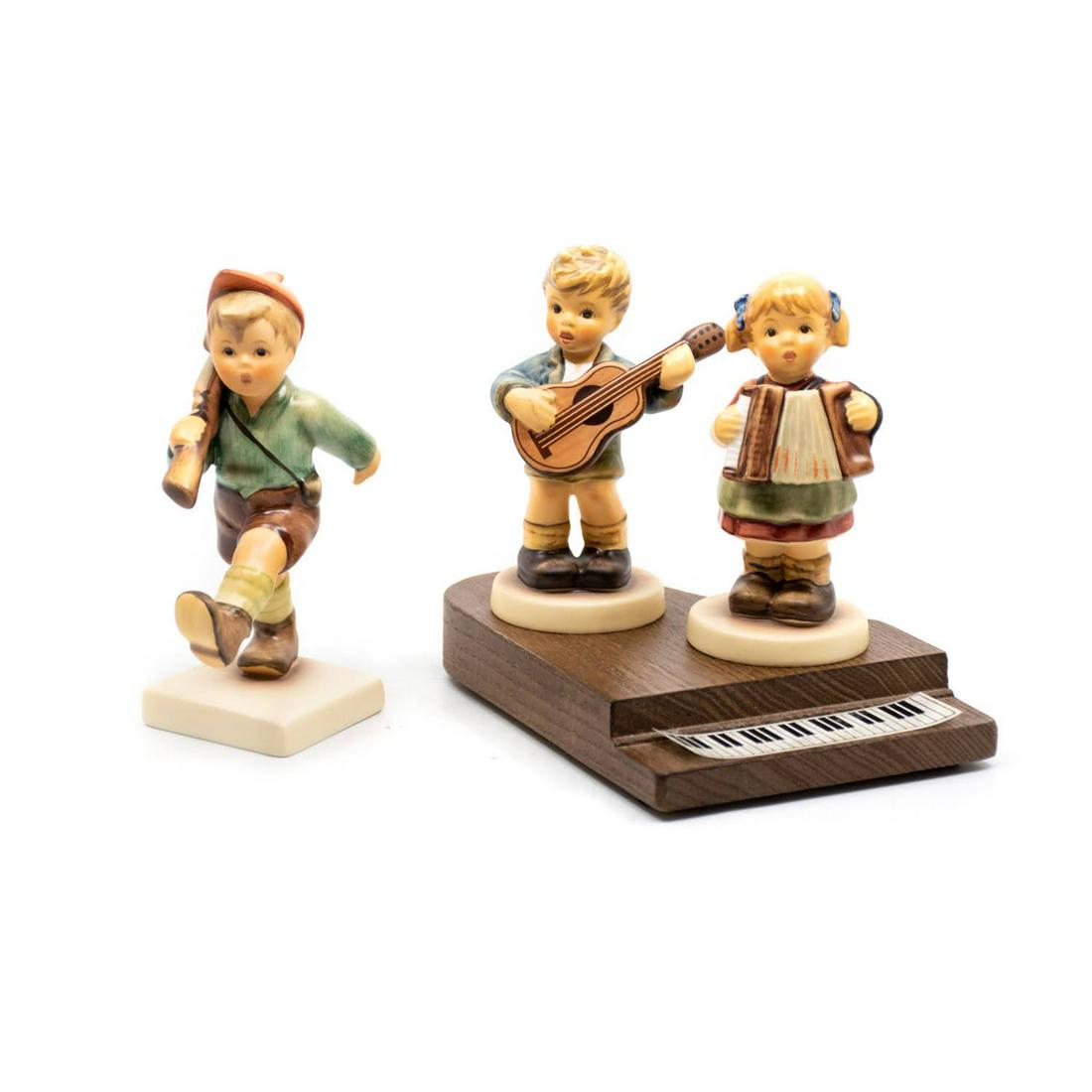 Goebel Hummel On Parade 720 and Serenade of Songs 2171: Goebel Hummel #720 On Parade TMK 7 features a marching boy carrying a rifle, #2171 A/B Serenade of Songs TMK 8 features a boy playing guitar and a girl playing accordion on a wooden piano base.