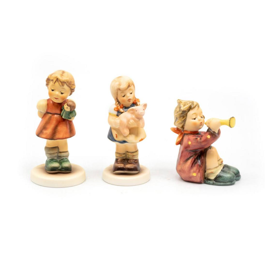 Group of 3 Goebel Hummels including Puppet Princess: Goebel Hummel #2103/A TMK 8 features a girl playing with a puppet, #2052 Pigtails TMK 7 features a girl with her hair in pigtails while carrying a pig, and #391 Girl with Trumpet TMK 6 features a sitt