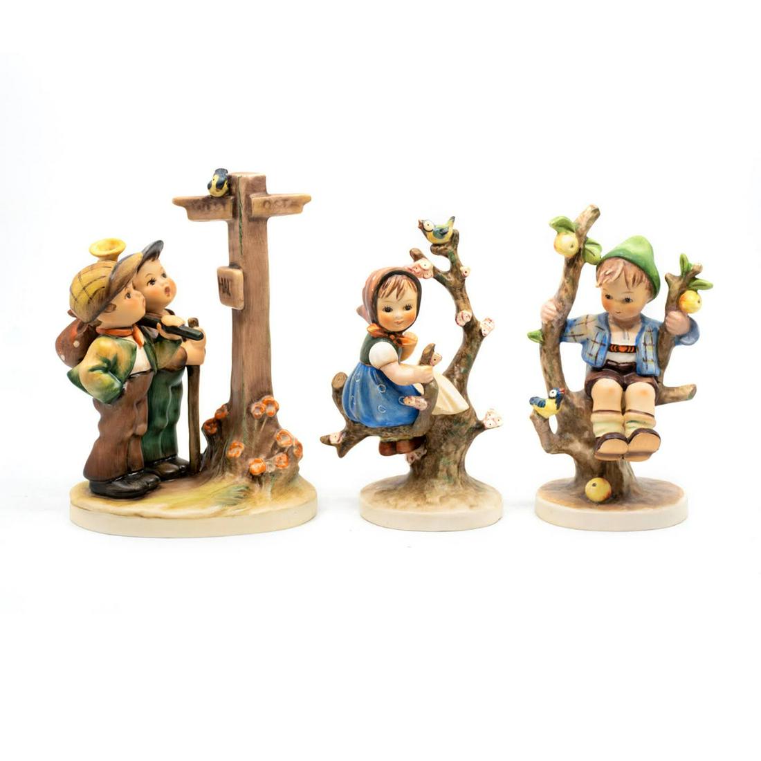 Group of 3 Goebel Hummels including Crossroads 331: Goebel Hummel #331 Crossroads TMK 5 features two hikers looking at a sign posted at the crossroads, #142 Apple Tree Boy TMK 3 features a boy sitting in an apple tree with a bird perched beside him, an