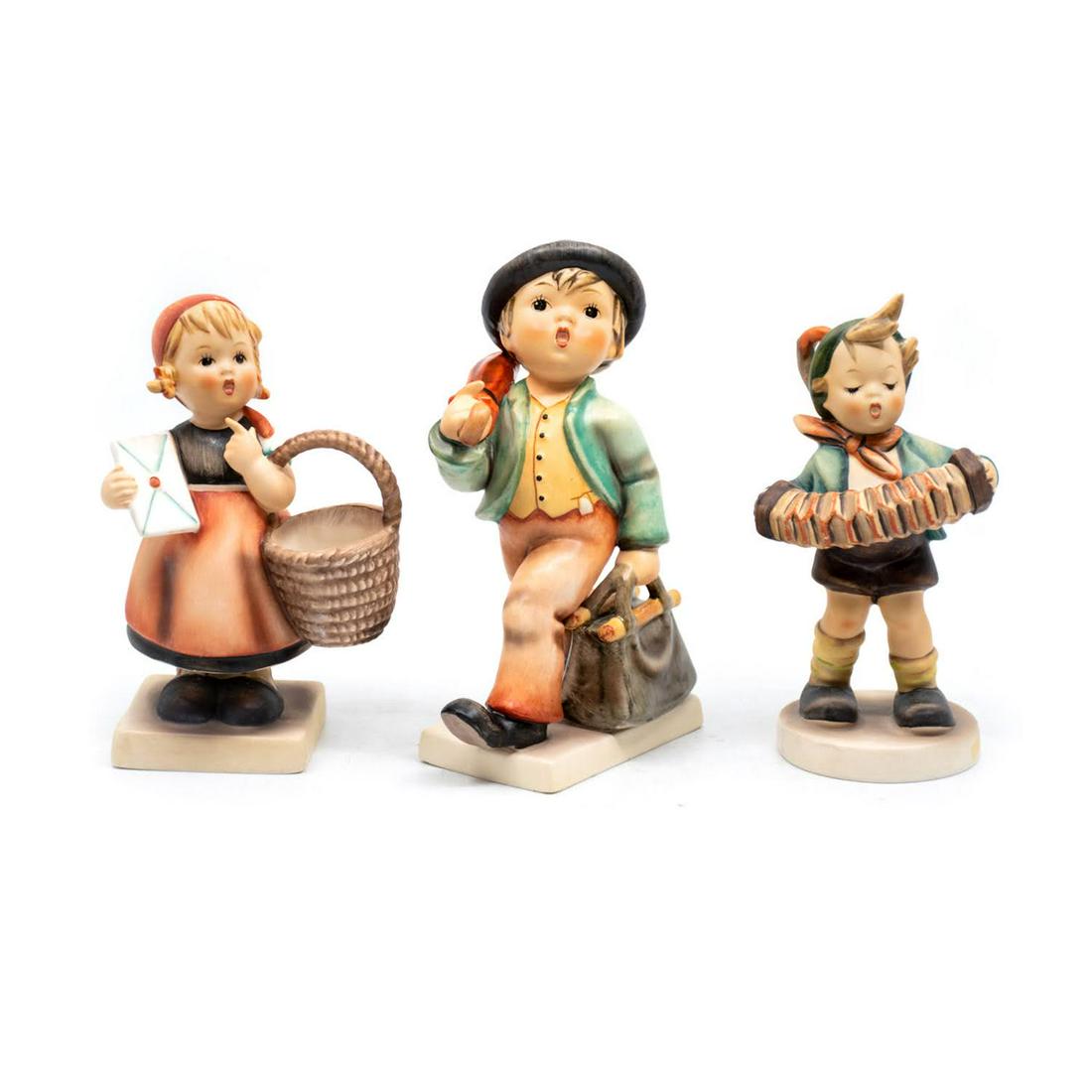 Group of 3 Goebel Hummels including Meditation 13: Goebel Hummel #13/0 Meditation features a girl carrying a letter and a basket, #7/0 Merry Wanderer TMK 3 features a boy carrying a case and an umbrella while walking, and #185 Accordion Boy TMK 5 feat