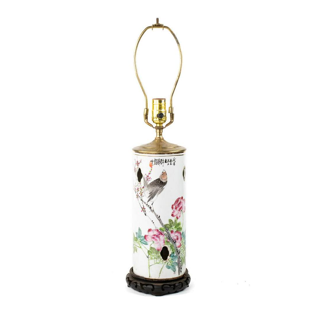 Chinese Famille Rose Porcelain Bird Motif Table Lamp: Chinese Famille Rose porcelain bird motif table lamp having cylinder form porcelain body with hand painted bird and floral motif and window cutouts. It features a brass cap and rests atop wood carved 