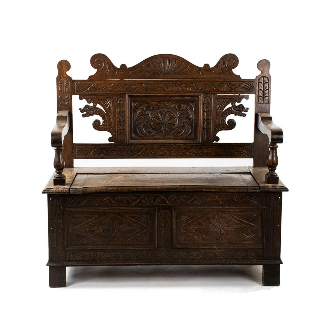 Italian Carved Figural Hall Bench: An Italian carved figural hall bench with heavily carved panels on the back rest and bottom featuring carved figure finials, lion head arm rests and claw feet. The bench seat lifts open for storage.