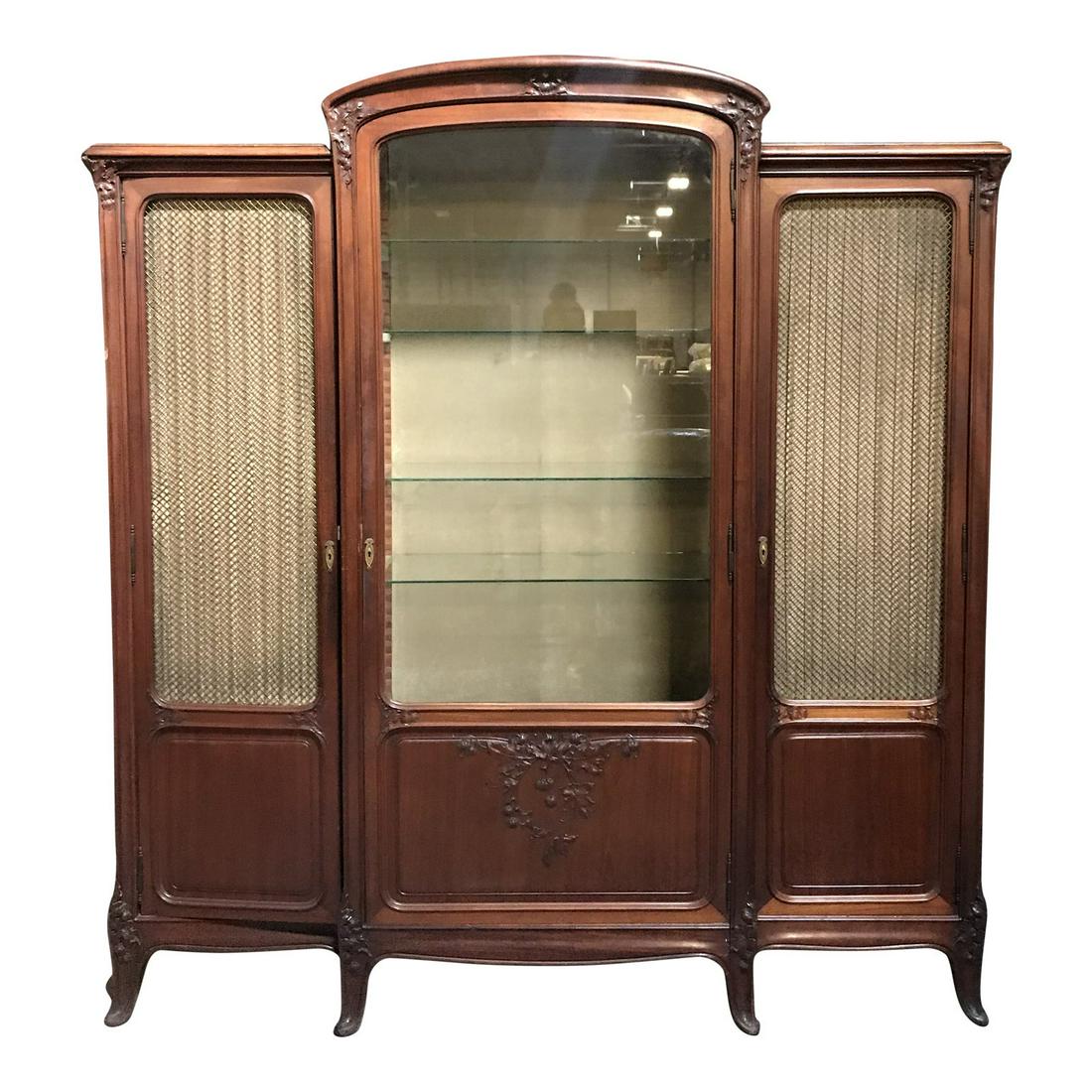 1920s Art Nouveau 3 Door Breakfront Armoire Cabinet: A 1920's Art Nouveau three door armoire and breakfront cabinet having large middle glass door flanked by two grille style doors with wire mesh paneling atop wood, all with brass keyholes and hardware.