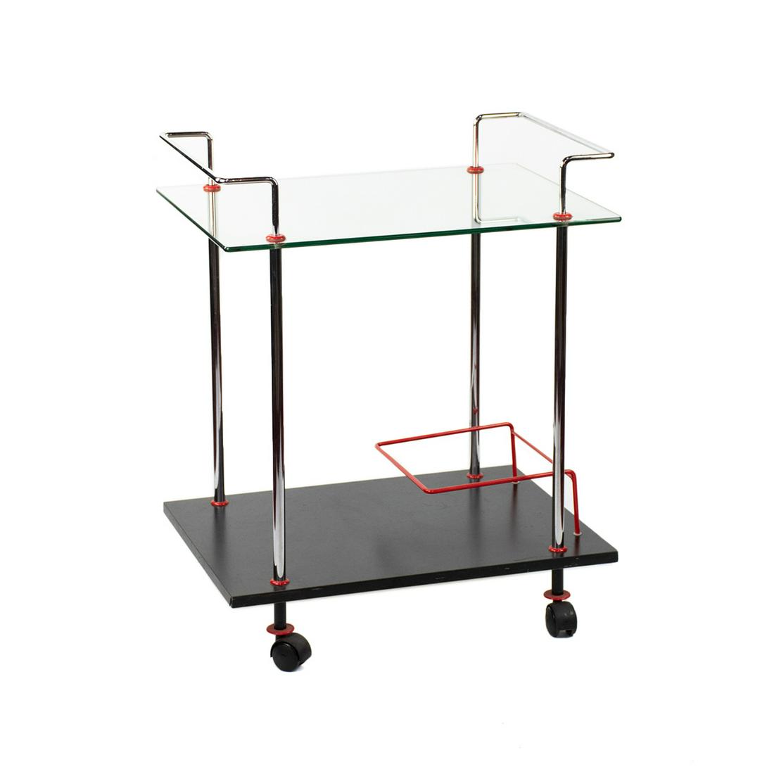 1980s Casprini Italian Glass and Chrome Bar Cart: A 1980s vintage Italian rolling bar cart by Casprini. This piece features a simplistic chrome construction with a glass top shelf, black veneer wooden bottom shelf, and red detailing. It rests atop fo