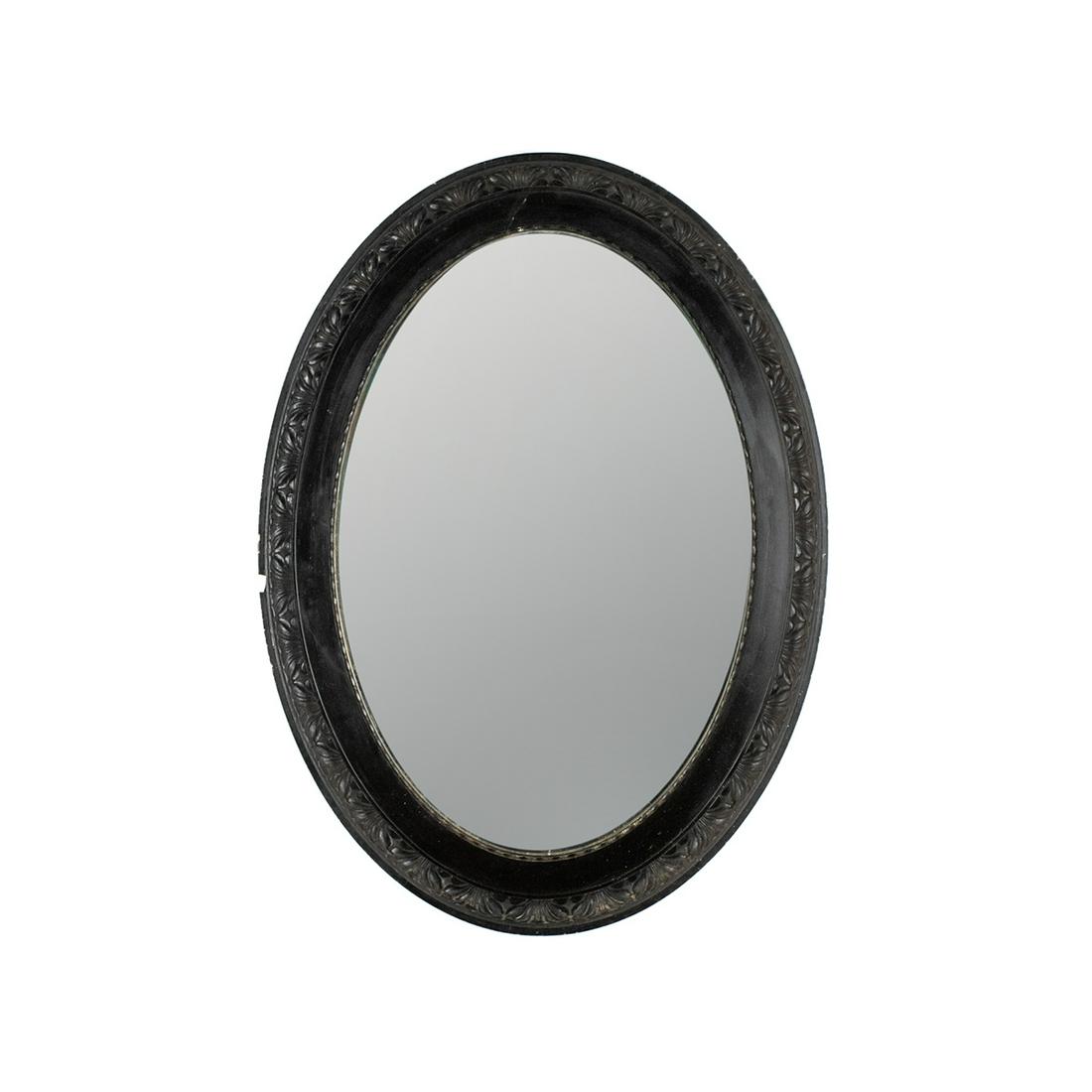 Antique Ebony Gesso Oval Wall Mirror: An antique turn of the century ebony black gesso oval wall mirror. The mirror glass features a beveled edge and the frame features foliate designs throughout. It is unmarked.