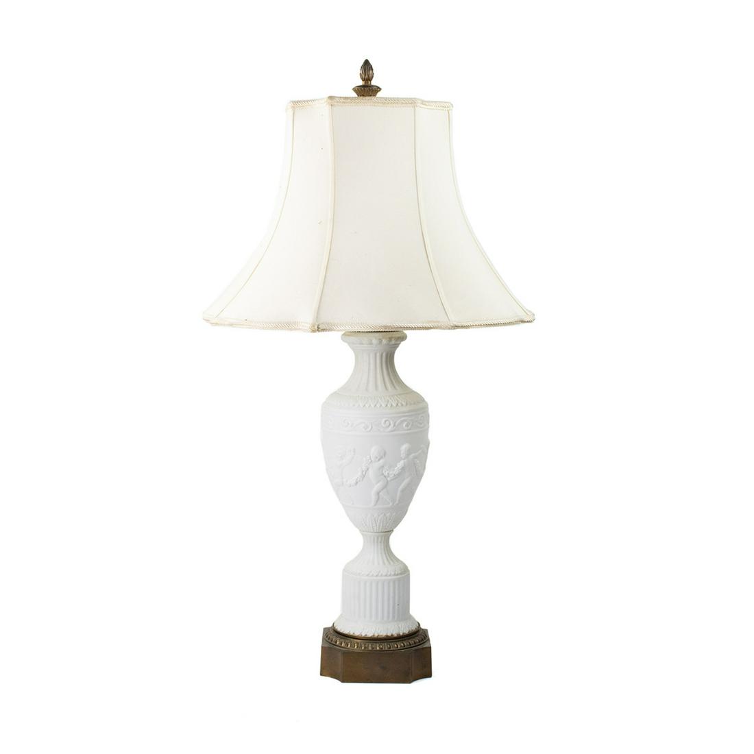 Neoclassical Style Bisque Cherub Motif Table Lamp: A vintage Neoclassical style bisque or biscuit porcelain Parian table lamp. This piece features an urn form with Roman column and cherub motifs throughout. It has a brass base, cap, and hardware. It i