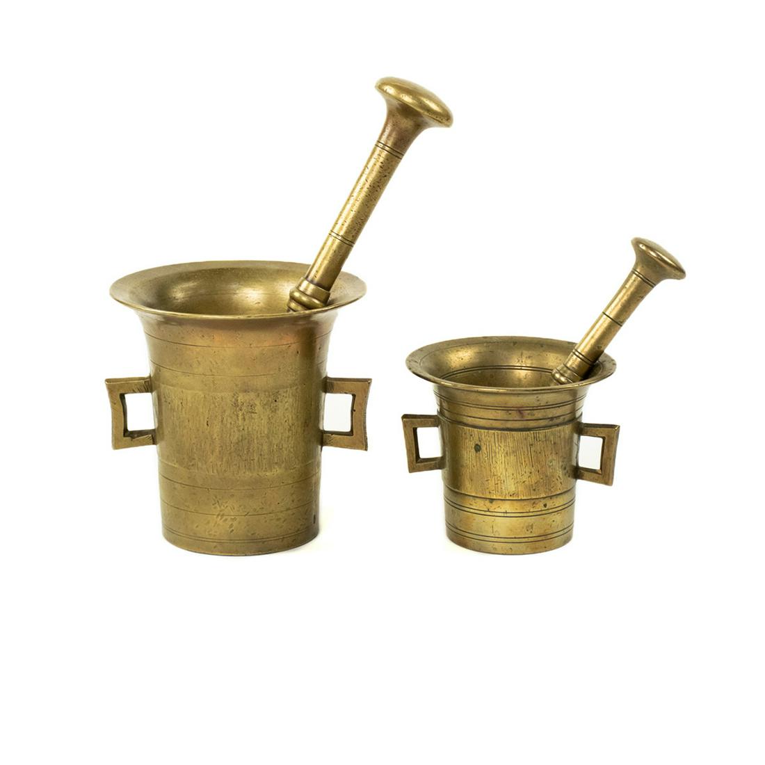 Antique Brass Mortar and Pestle Sets: A pair of antique brass mortar and pestle sets. Each features engraved rings around the body the and squared handles. They are unmarked.
