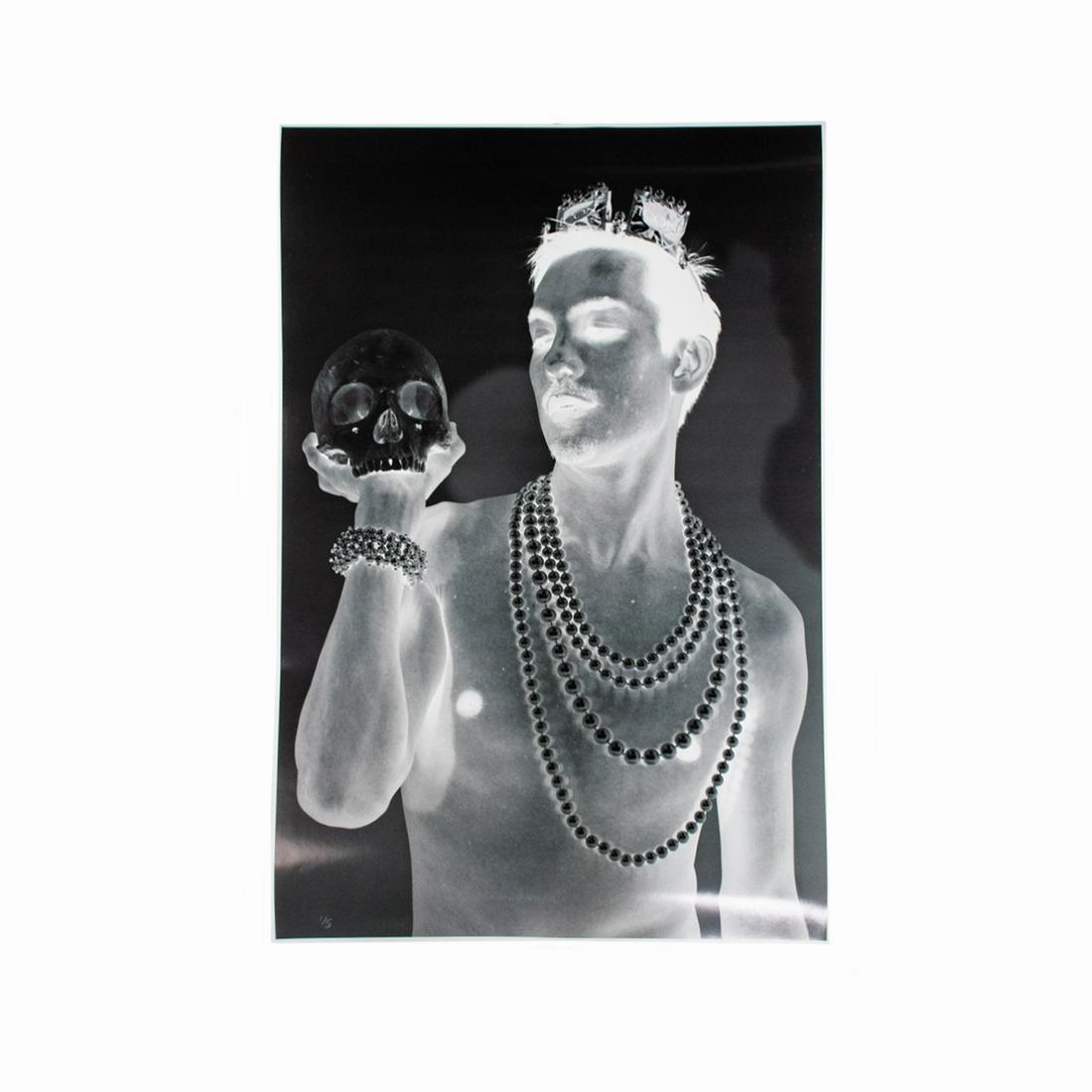 Signed Black and White Negative Photograph - 1/5: A limited edition black and white negative photograph. This work depicts a male subject wearing Mardi Gras beads while holding up a human skull in one hand. It is signed illegibly on the lower right a