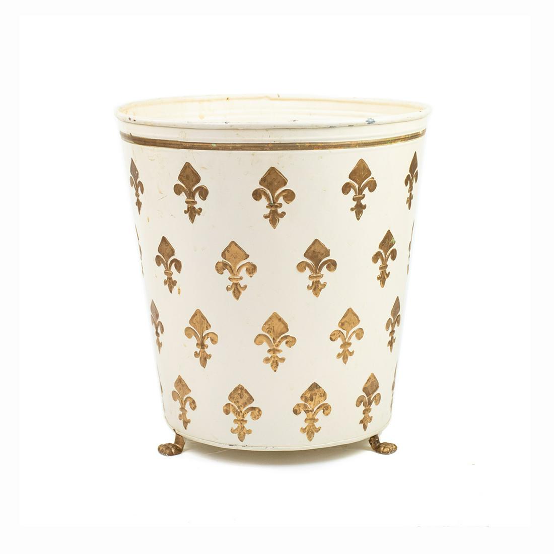 Mid-Century Fleur de Lis Toleware Waste Bin: A vintage Mid-Century toleware waste bin. This piece features a repeating gilt fleur de lis design throughout over a cream base. It rests atop gold-tone lion paw feet. It is unmarked.