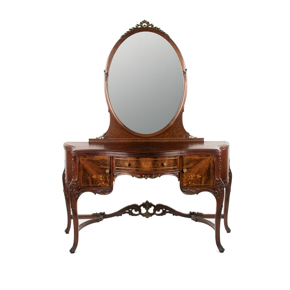 Continental Flame Mahogany Vanity Dressing Table: A Continental style flame mahogany vanity dressing table featuring ornate carved detailing with gilt accents, inlaid floral designs, one center drawer, four side drawers concealed by hinged doors, an