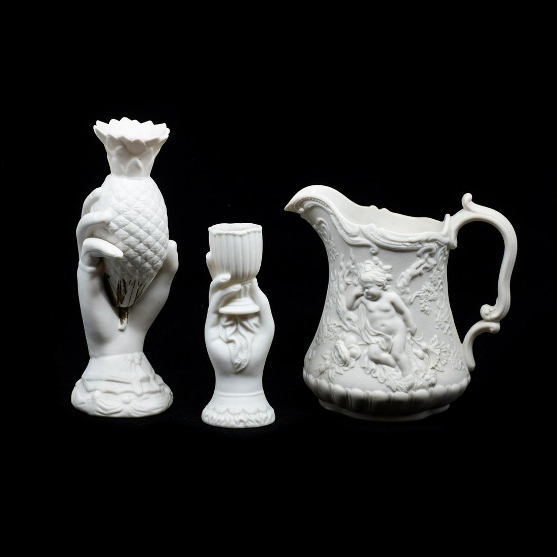 19th C. Parian Bisque Pieces: A grouping of three 19th century antique parian bisque porcelain pieces, including a hand holding a corn cob form vase, a hand holding a goblet form vase, and a cherub motif pitcher. They are unmarked
