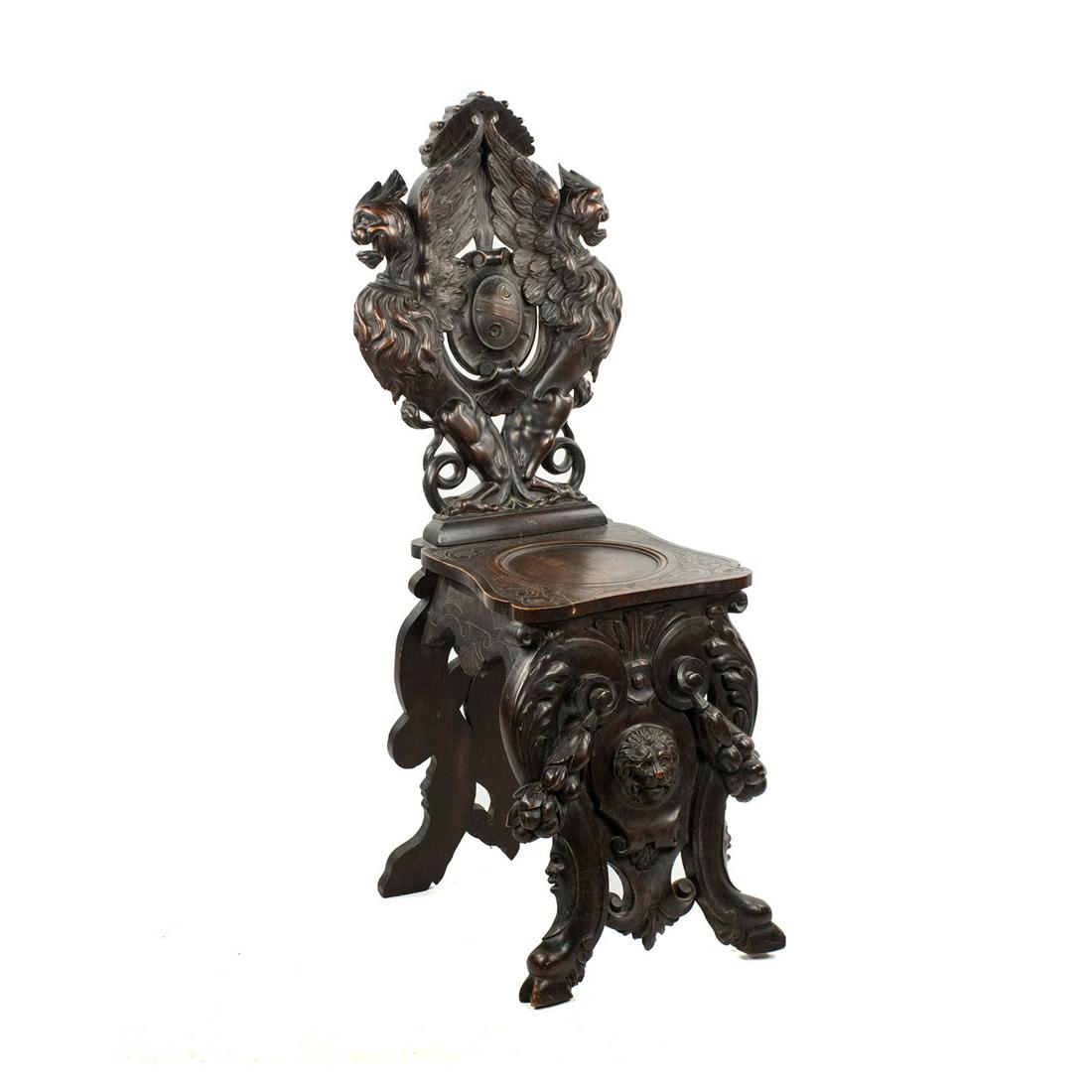 Italian Renaissance Style Carved Hall Chair: Italian Renaissance style walnut hall chair featuring a heavily carved body with lion, shield, and foliate motifs throughout. It is unmarked.