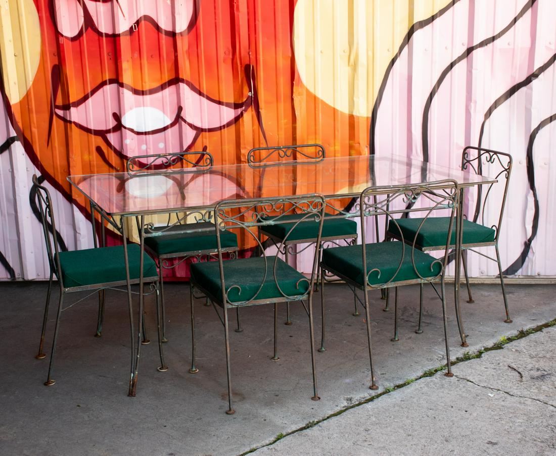 Woodard Iron Dining Table and Chairs Set: A vintage Woodard iron patio table and chairs set. The table features simplistic swirl motifs to the frame, a rectangular glass top, and curved legs. The six chairs feature a corresponding design and