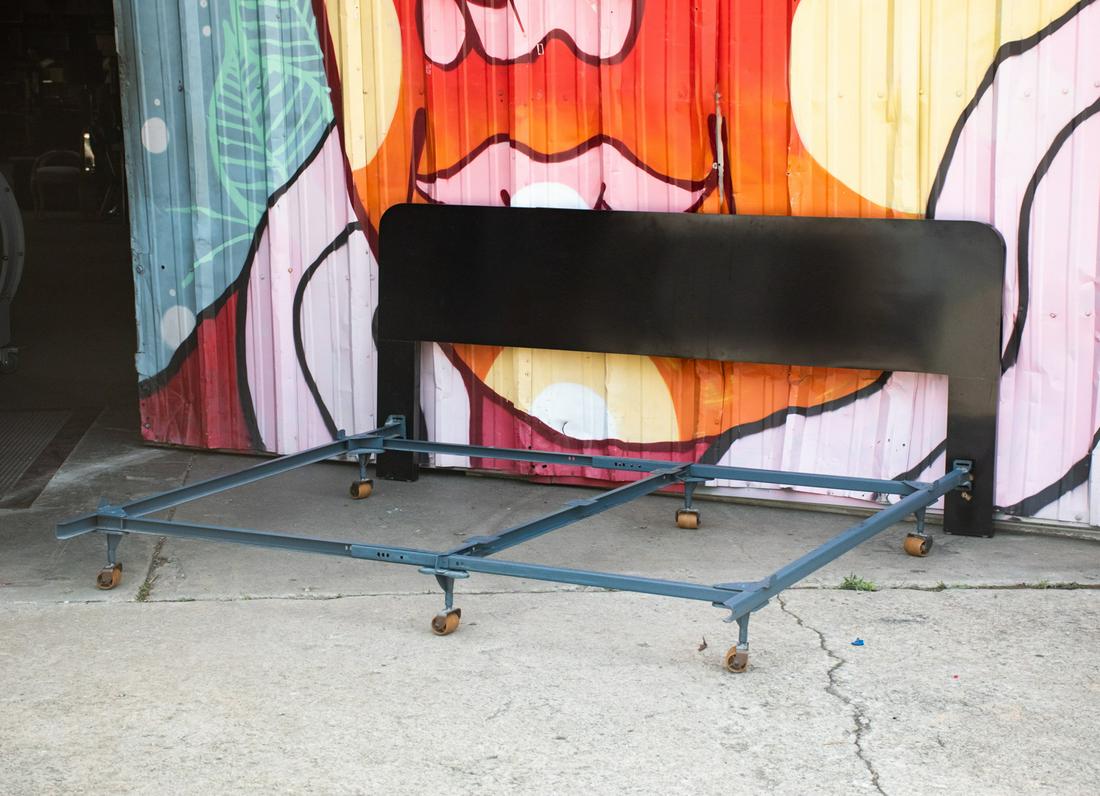 Modern Black Laminate King Headboard after Karl: An early 80's Memphis Group style Postmodernist black veneer laminate waterfall deco king size headboard with adjustable metal frame with wheels. Headboard attaches to frame. Unmarked.