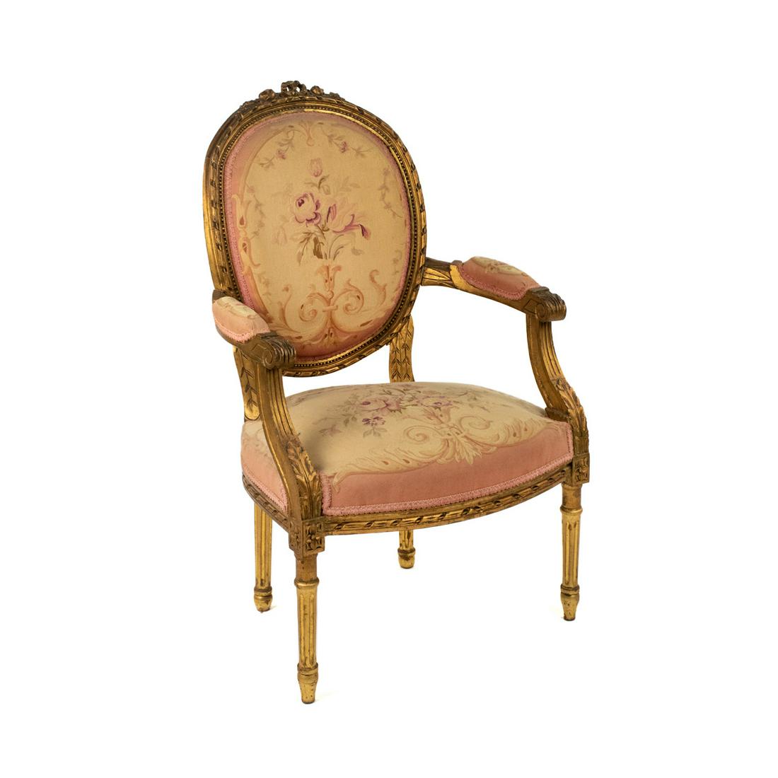 French Louis XVI Style Petipoint Fauteuil Gilt Armchair: A French Louis XVI style gilt and floral petipoint tapestry upholstered fauteuil armchair having pink floral upholstery on the back rest, arm cushions and seat. It features carved ribbon form back wit