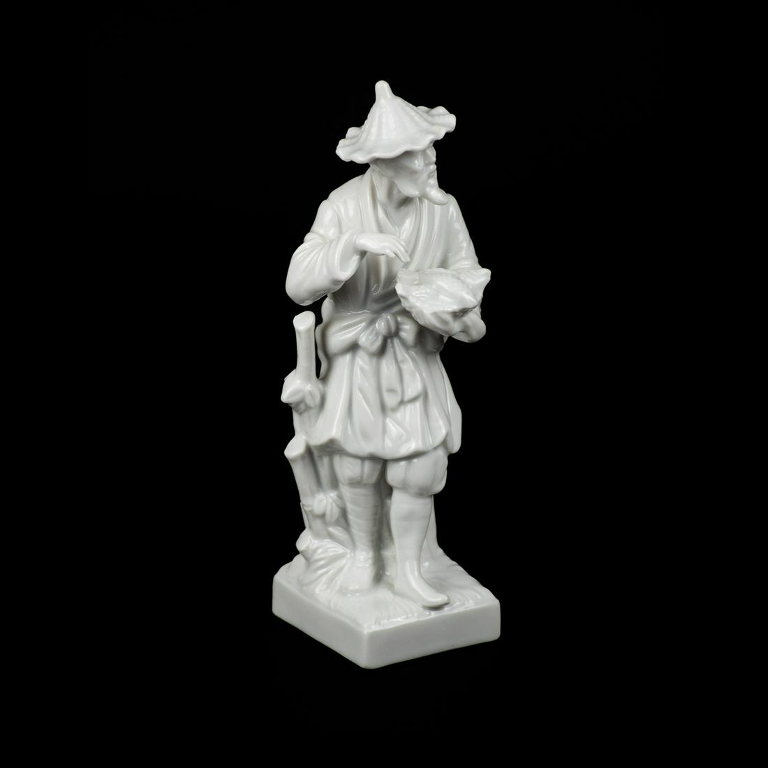 Fitz & Floyd Blanc-de-Chine Chinese Fisherman Figure: A Fitz and Floyd Blanc de Chine Chinese fisherman figure depicting a man with a hat and basket of fish in his hand resting atop a square base. Marked on underside "Fitz and Floyd MCMIXXVI P22/21W".