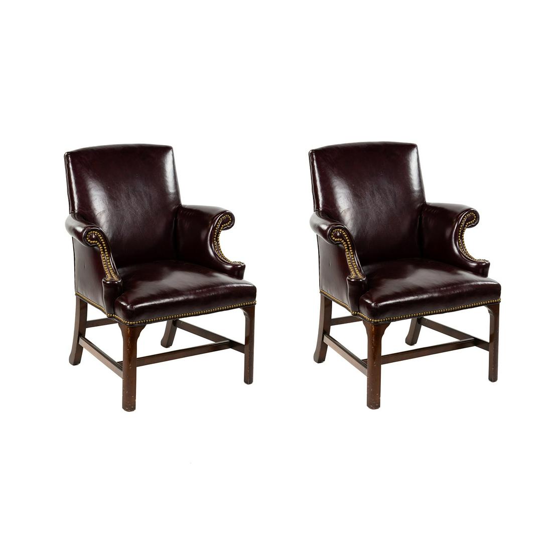 Pair of English Burgundy Leather Library Armchairs: A pair of English burgundy leather library reading armchairs having rolled arms with square wooden bases and clad nail border on arms and seat bases. Seat height: 17.5"