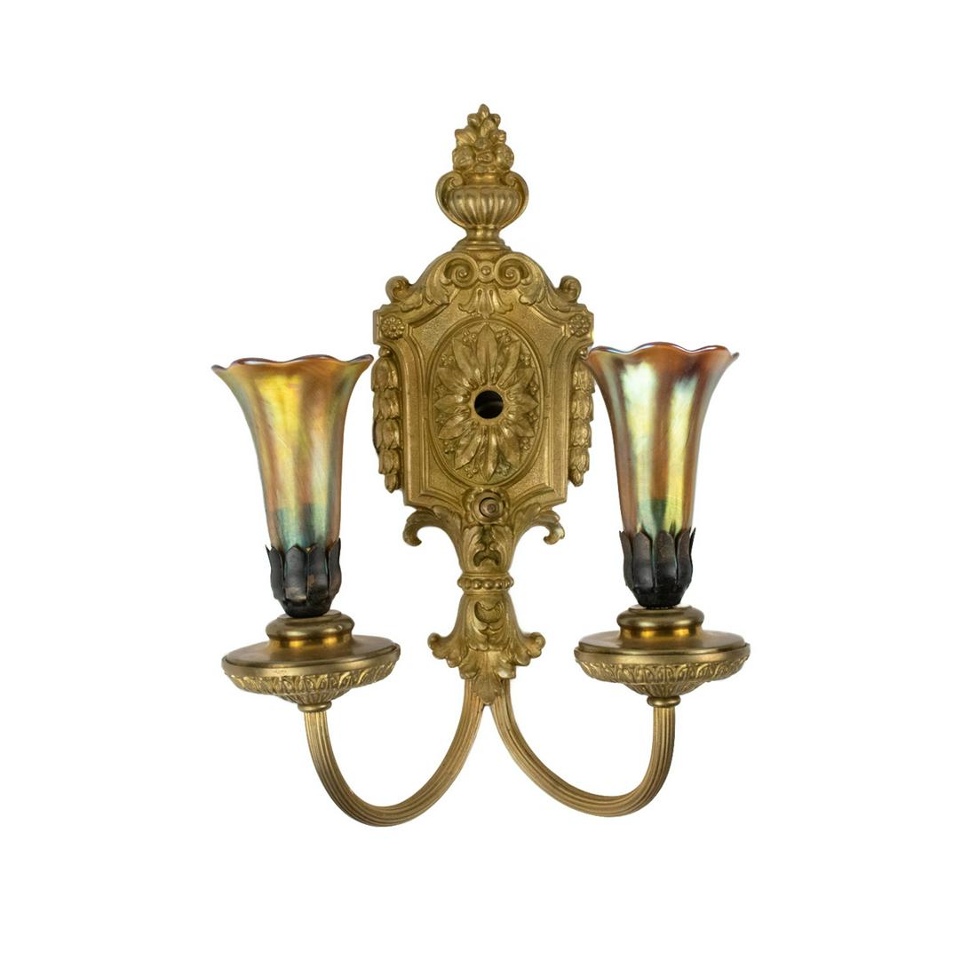 Tiffany Style Two Light Lily Shade Sconce: A Tiffany Style bronze two arm sconce with acanthus and floral design and two favrile gold iridescent lily shades. Sconce is impressed Tiffany Studios New York and shades are incised L.C.T. Shades are