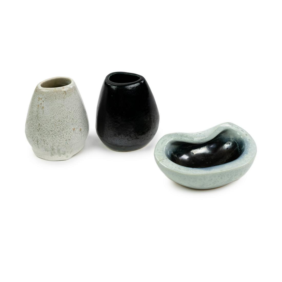 (3) Group of Russel Wright Corsage Vases and Ashtray: A grouping of Russel Wright for Bauer glazed stoneware including two Corsage vases, one in gunmetal black and one in an off-white speckle, and a dark blue to light blue glazed clam form or pinched ash